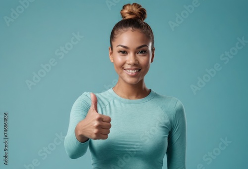 Young woman in a teal top giving a thumbs up, her top bun hairstyle adds to the casual yet confident vibe.