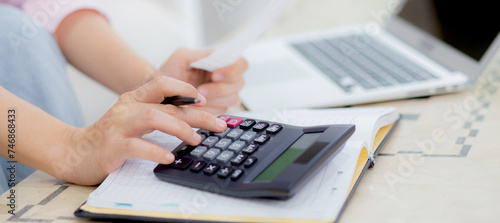 Closeup hands of woman calculating finance household with calculator on desk at home, girl checking bill for saving and planning expenses, debt and loan, tax and accounting, business and financial.