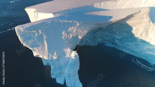 Giant Antarctic blue iceberg cave in sunset bright light. Huge crashed ice glacier at polar nature environment. Ecology, melting ice, climate change and global warming concept. Aerial drone panorama photo