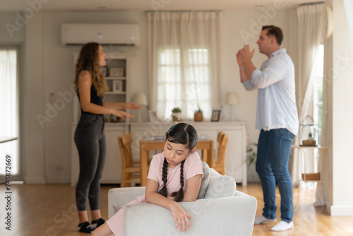 Annoyed and unhappy young girl sitting on sofa trapped in middle of tension by her parent argument in living room. Unhealthy domestic lifestyle and traumatic childhood develop to depression.Synchronos