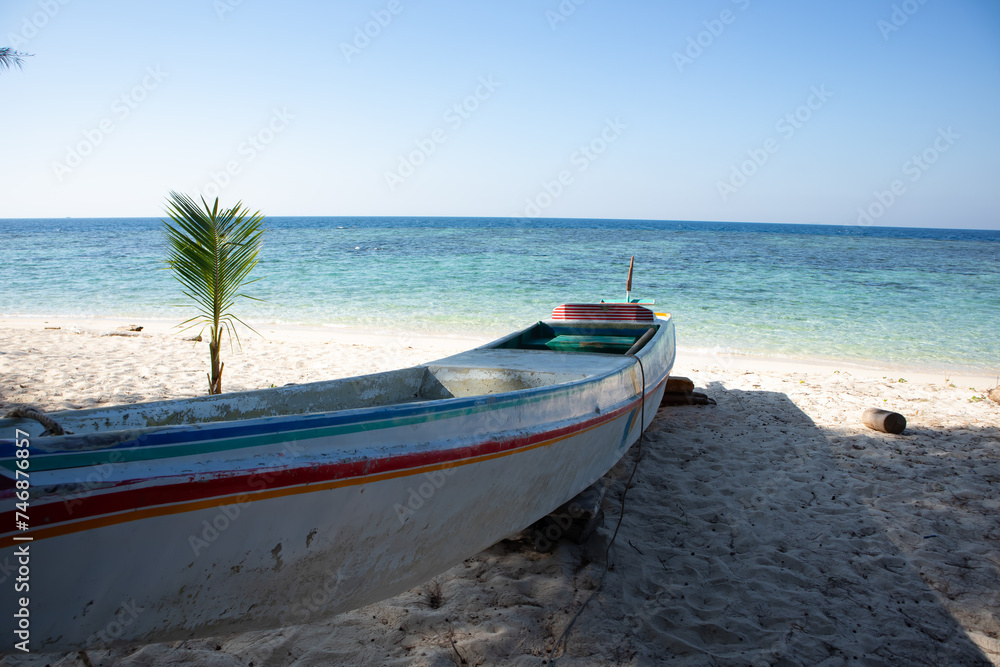 a wooden boat sitting on top of a sandy beach with blue sea background at karang panambungan island south sulawesi Indonesia a wooden boat sitting on top of a sandy beach with blue sea background at karang panambungan island south sulawesi Indonesia