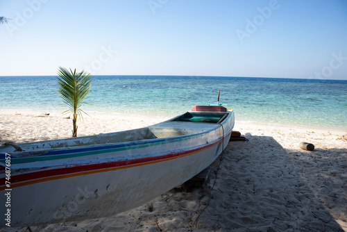 a wooden boat sitting on top of a sandy beach with blue sea background at karang panambungan island south sulawesi Indonesia