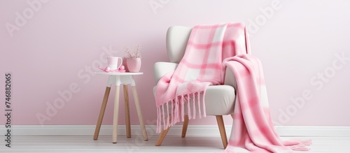 A white stool chair is topped with a giant pink plaid woolen blanket in a Scandinavian style home. The chairs clean lines and minimalist design complement the cozy texture of the blanket.