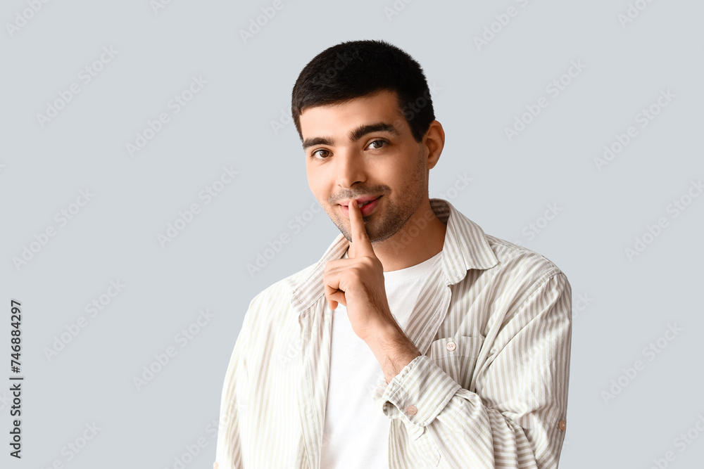 Young man showing silence gesture on light background Young man showing silence gesture on light background