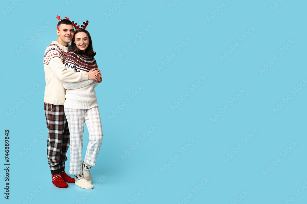 Fototapeta premium Happy young couple in Christmas pajamas hugging on blue background