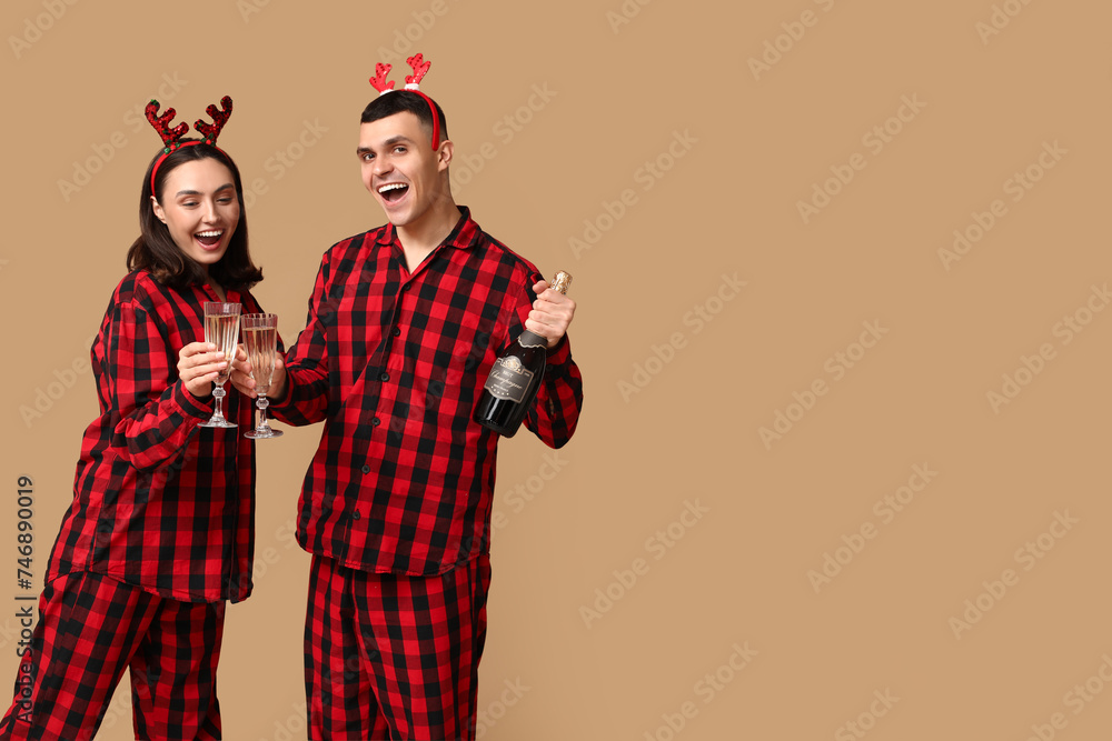 Happy young couple in Christmas pajamas and with champagne on beige background Happy young couple in Christmas pajamas and with champagne on beige background