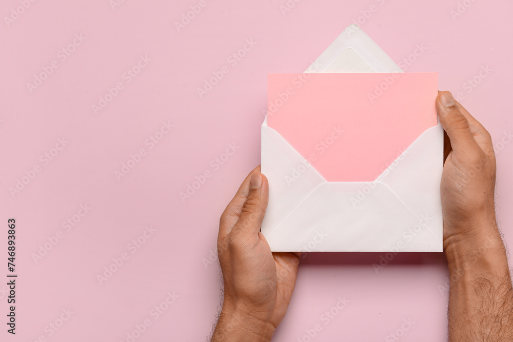 Male hands with envelope and blank card on pink background. Valentine's Day celebration Male hands with envelope and blank card on pink background. Valentine's Day celebration