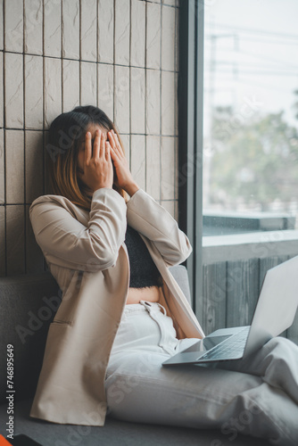 Quadro em tela Visibly upset businesswoman covers her face, seeking a moment of respite from the stresses of work with a laptop beside her