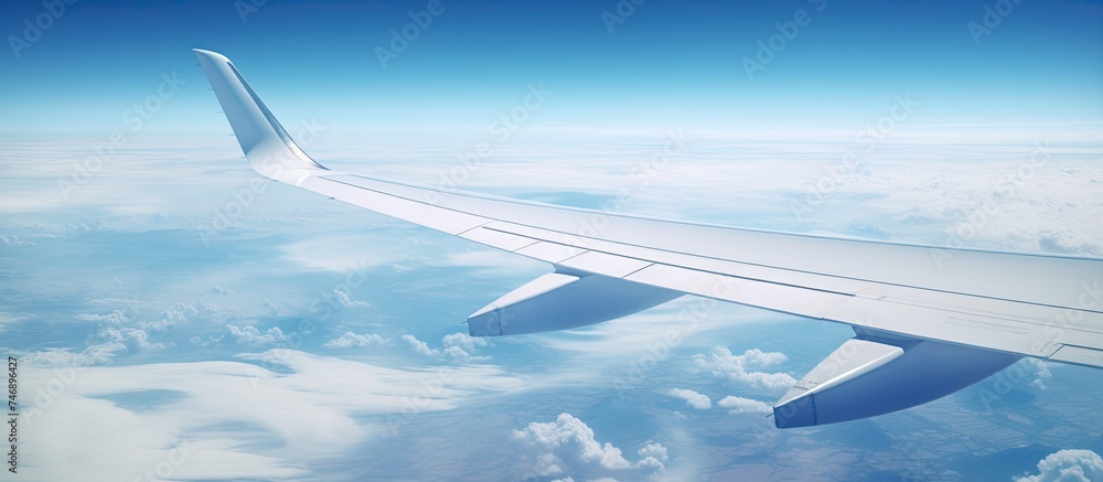 Obraz premium An aerial shot capturing a commercial jet planes wing above fluffy clouds with the Pacific Ocean visible below. The wing is turning upwards on the left side of the frame.