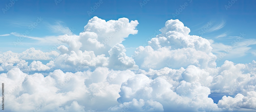 Naklejka premium A plane can be seen soaring through a vivid blue sky filled with fluffy white clouds. The aircraft stands out against the backdrop of the dynamic cloud formations as it navigates through the