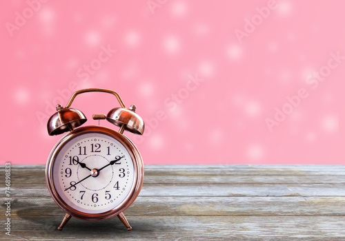 Vintage alarm clock on wood table with pink bokeh light as background.