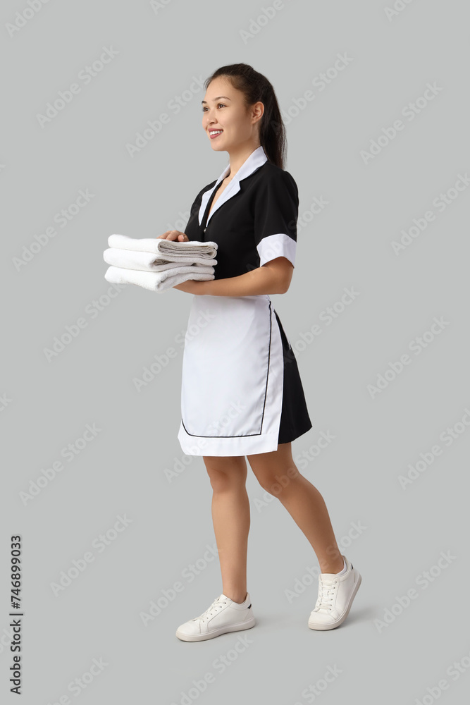 Young Asian chambermaid with clean towels on light background Young Asian chambermaid with clean towels on light background