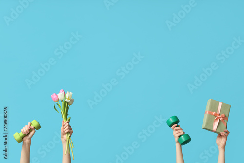 Female hands with dumbbells, gift box and tulips for International Women's Day on color background photo