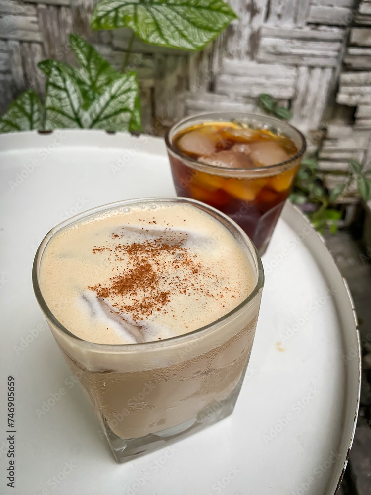 A glass of iced coffee and caffe latte drinks on a wooden table with houseplants background. Black coffee with ice cubes on the surface of the drink. Americano Long Black and Milk Coffe. A glass of iced coffee and caffe latte drinks on a wooden table with houseplants background. Black coffee with ice cubes on the surface of the drink. Americano Long Black and Milk Coffe.