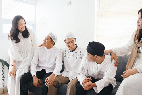 Young Asian muslim friends, man and woman, sitting, talking and laughing together during Ramadan or Eid mubarak celebration photo