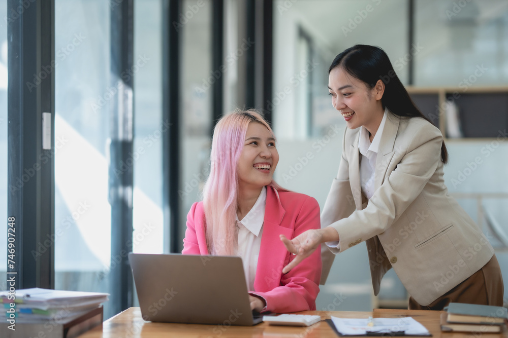 Two asian business woman working together on a project in a modern office. Teamwork and partnership concept. Two asian business woman working together on a project in a modern office. Teamwork and partnership concept.