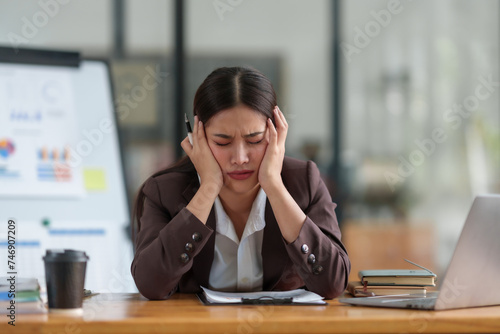 Stressed asian businesswoman with headache working at laptop in office. Stress and health at work concept.