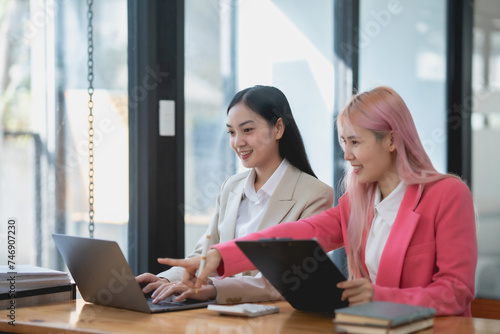 Two asian business woman working together on a project in a modern office. Teamwork and partnership concept. © amnaj