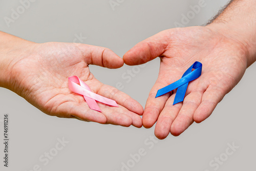 Two hands holding two Pink and Blue ribbons for the Pink October and Blue November campaigns to support life and raise awareness about cancer. Man's hand and woman's hand