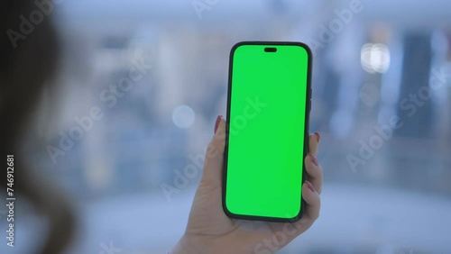 Close-up of a woman's hand holding a mobile phone with a green screen mockup. A woman is in an elevator in a shopping center 4K