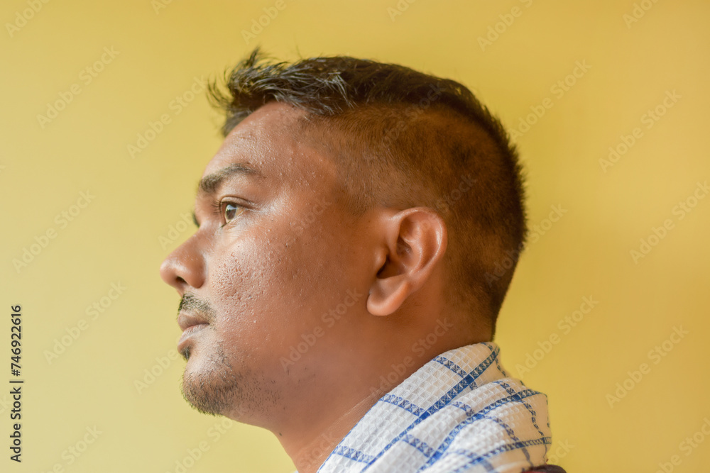 Obraz premium Side view of a young Indian man isolated on a yellow background with a fresh hairstyle. Barbershop photo of a client after a haircut.