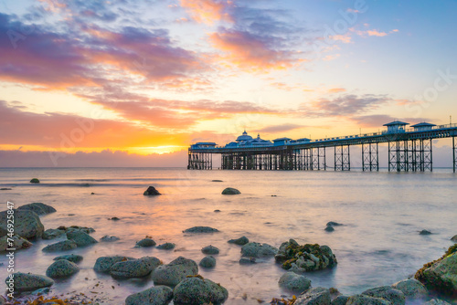 Vibrant colorful sunrise over the rugged rocky coastline with Llandudno Pier in the background - North Wales, United Kingdom photo