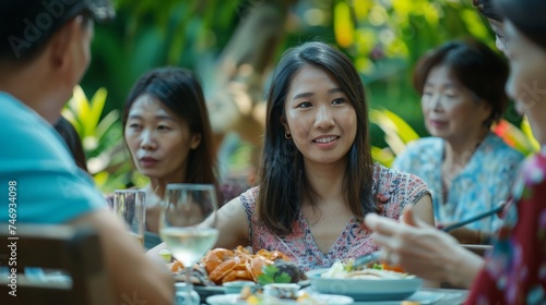 Young Asian women visit the family during parties outdoors in the garden. An attractive diverse group of people having dinner  eating food  and celebrating weekend reunion gathered at the dining table