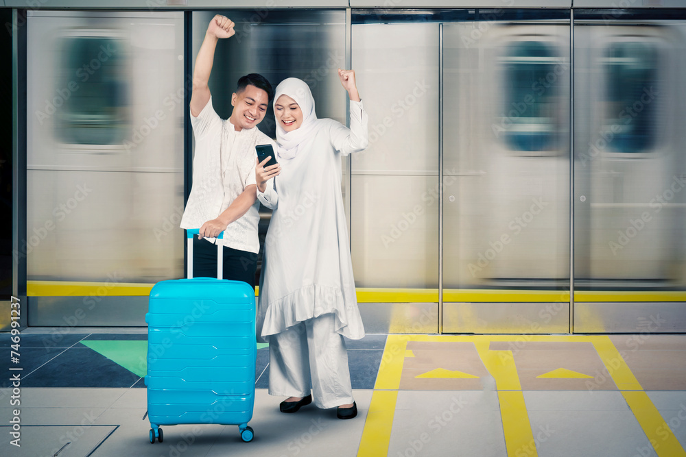 Muslim couple with suitcase showing thumbs up while looking at a mobile phone