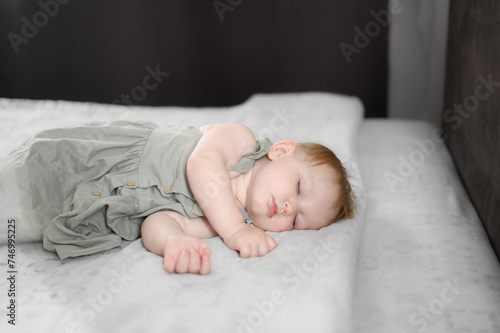 One-year-old child sleeps sweetly in a bed in the bedroom during lunchtime nap. Childhood, parenthood, health concept