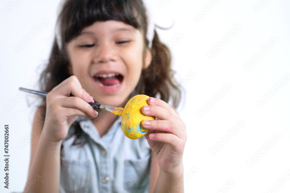 Little girl paints Easter eggs on white background, selective focus Little girl paints Easter eggs on white background, selective focus