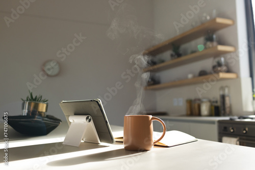 Steam rises from a coffee mug next to a tablet on a kitchen counter with copy space