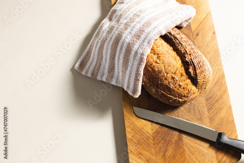A freshly baked loaf of bread rests on a wooden cutting board beside a knife, with copy space