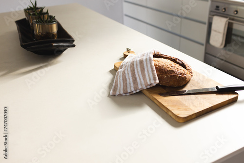A loaf of bread is partially covered with a striped cloth on a kitchen counter with copy space