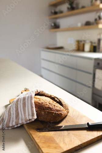 A loaf of bread rests on a wooden cutting board, partially covered by a striped towel, with copy spa
