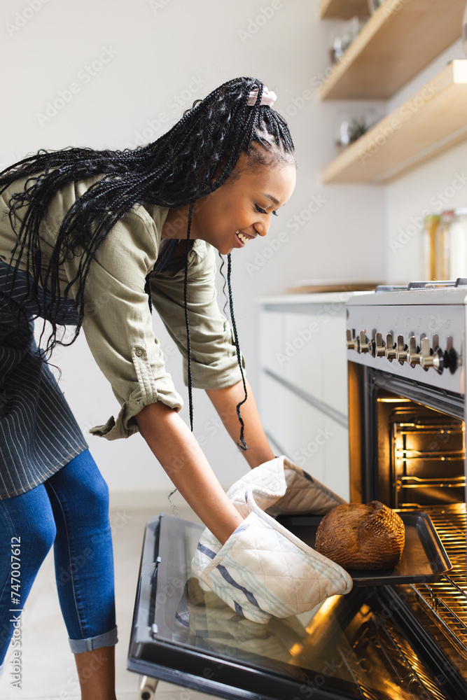 Fototapeta premium A young African American woman takes a loaf of bread out of an oven