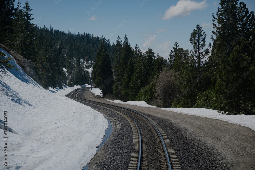 Curving train tracks wind through the Sierra Nevada mountains, approaching the rural town of Truckee, California. Snowy mountainsides and an evergreen pine forest surround the tracks. Curving train tracks wind through the Sierra Nevada mountains, approaching the rural town of Truckee, California. Snowy mountainsides and an evergreen pine forest surround the tracks.