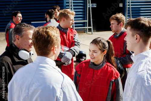 Pit crew with team principle standing in the pit lane talking  