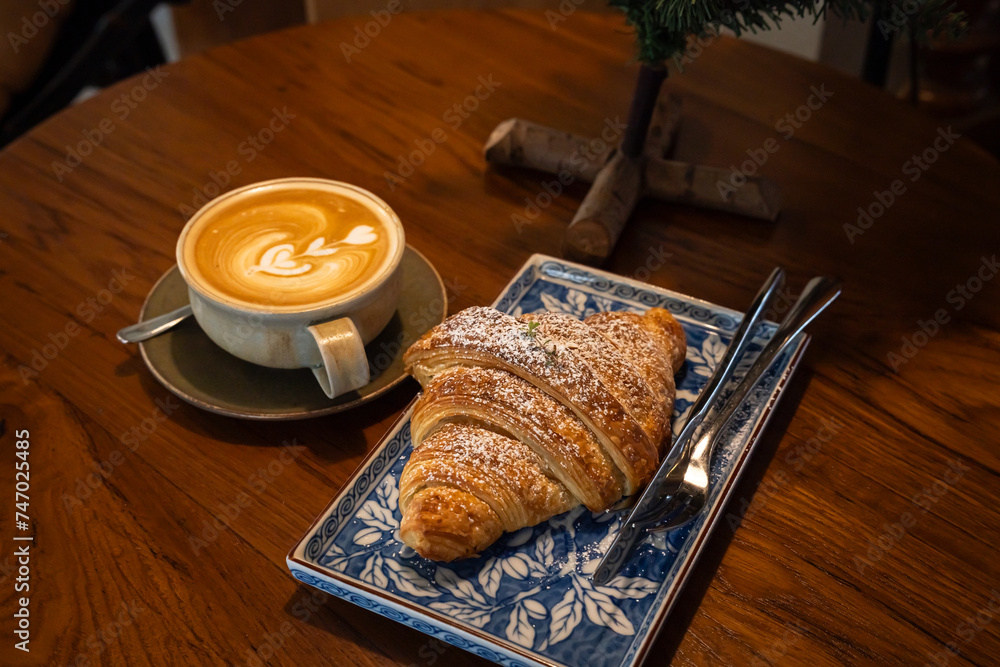 Hot coffee latte with latte art milk foam in cup mug with Croissant on wood desk on top view. As breakfast In a coffee shop at the cafe,during business work concept,vintage style