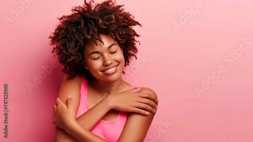Self care and love concept. Happy African American woman portrait hugging herself with pink background