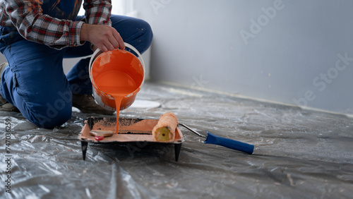 Close-up of man pours paint into the tray. Professional interior construction worker pouring orange color paint to tray. photo
