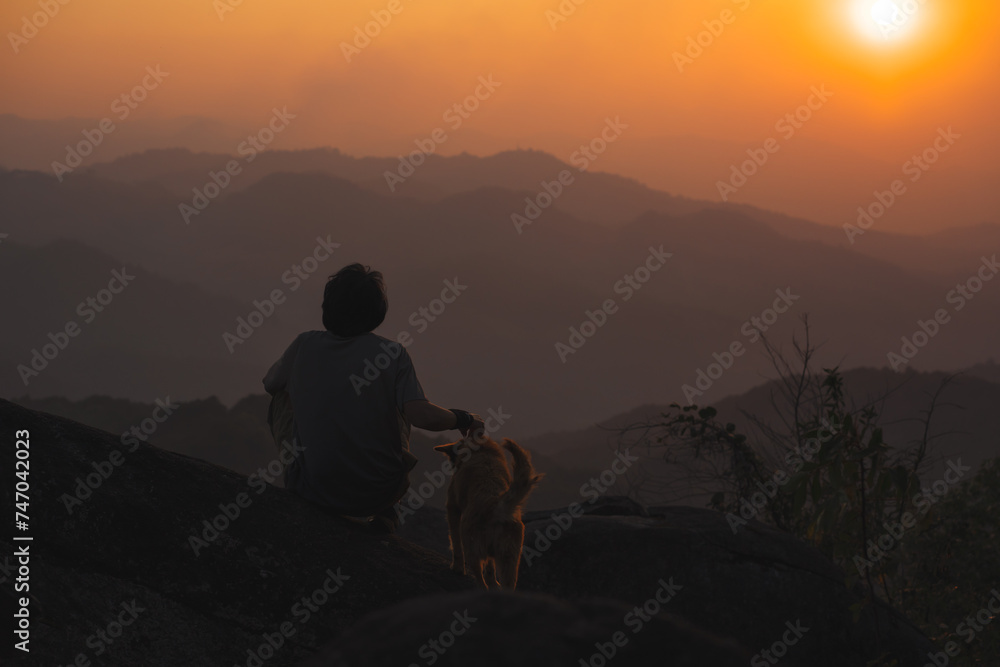 Obraz premium landscape and travel concept with solo freelancer man relax and play with dog at top of mountain and sunset with layer of mountain