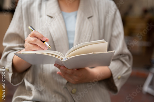 A businesswoman holding her notebook and taking notes in it, listing her ideas.