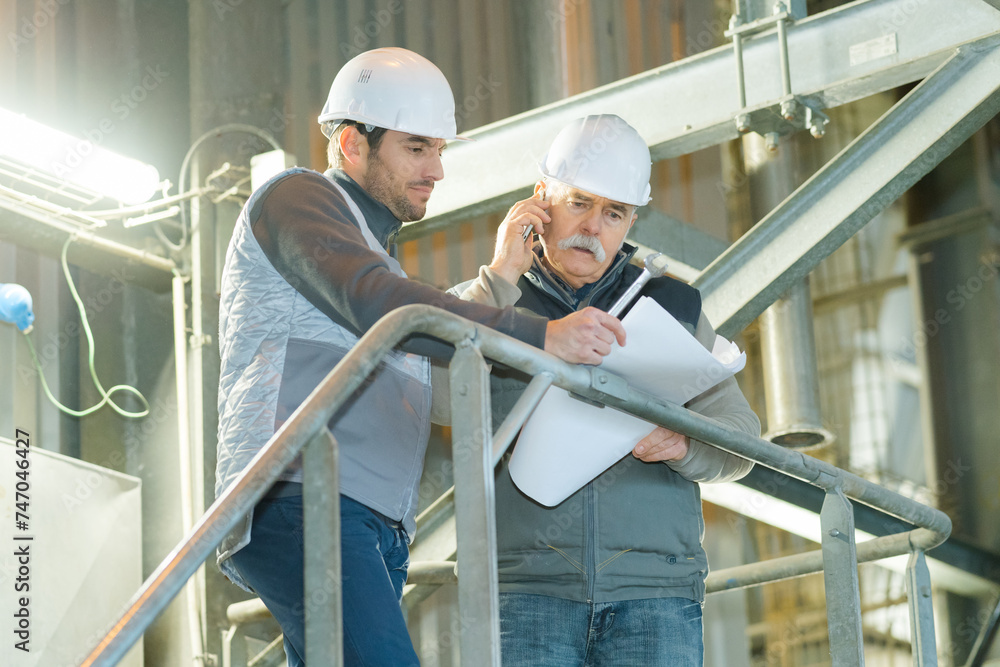 senior engineer and worker are talking with papers in factory