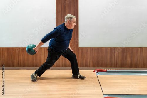 Elderly man poised to roll bowling ball in leisurely game, active senior lifestyle.