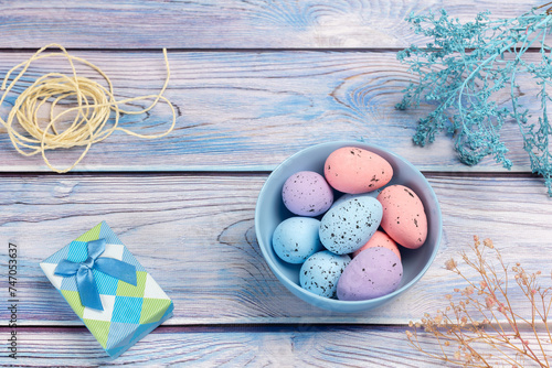 Bowl with colored Easter eggs and a gift box on the wooden background.