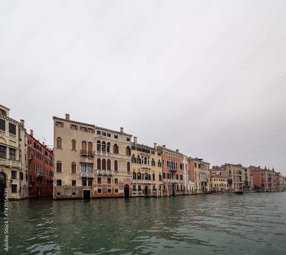 Facades of weathered buildings with windows on street of Venice city near canal water in daylight