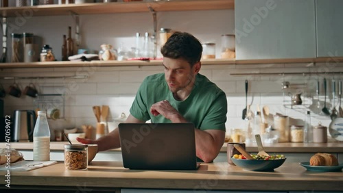 Pensive freelancer texting laptop at home kitchen closeup. Man eating breakfast photo