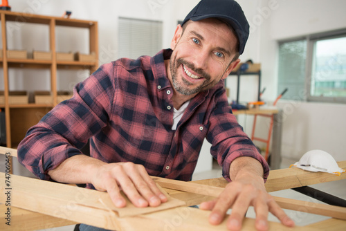 happy male carpenter sanding wood in his workshop