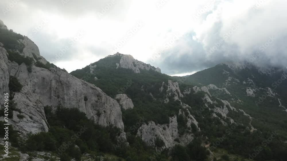 Drone flight towards the mountains in Croatia's Velebit National Park on a cloudy morning. Sun peeking behind the mountains. Drone flight towards the mountains in Croatia's Velebit National Park on a cloudy morning. Sun peeking behind the mountains.