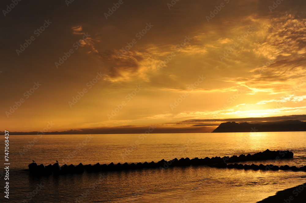 Sunset over the sea or ocean with a breakwater and clouds